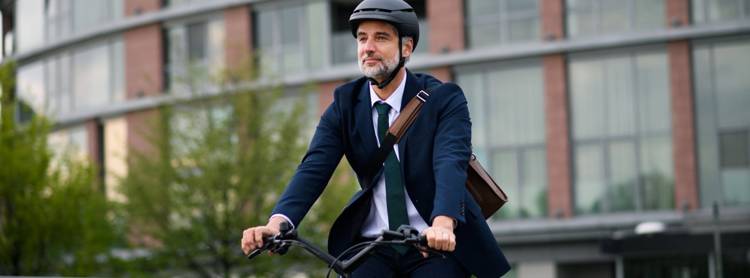En mand med cykelhjelm og taske over skulderen cykler på sin cykel