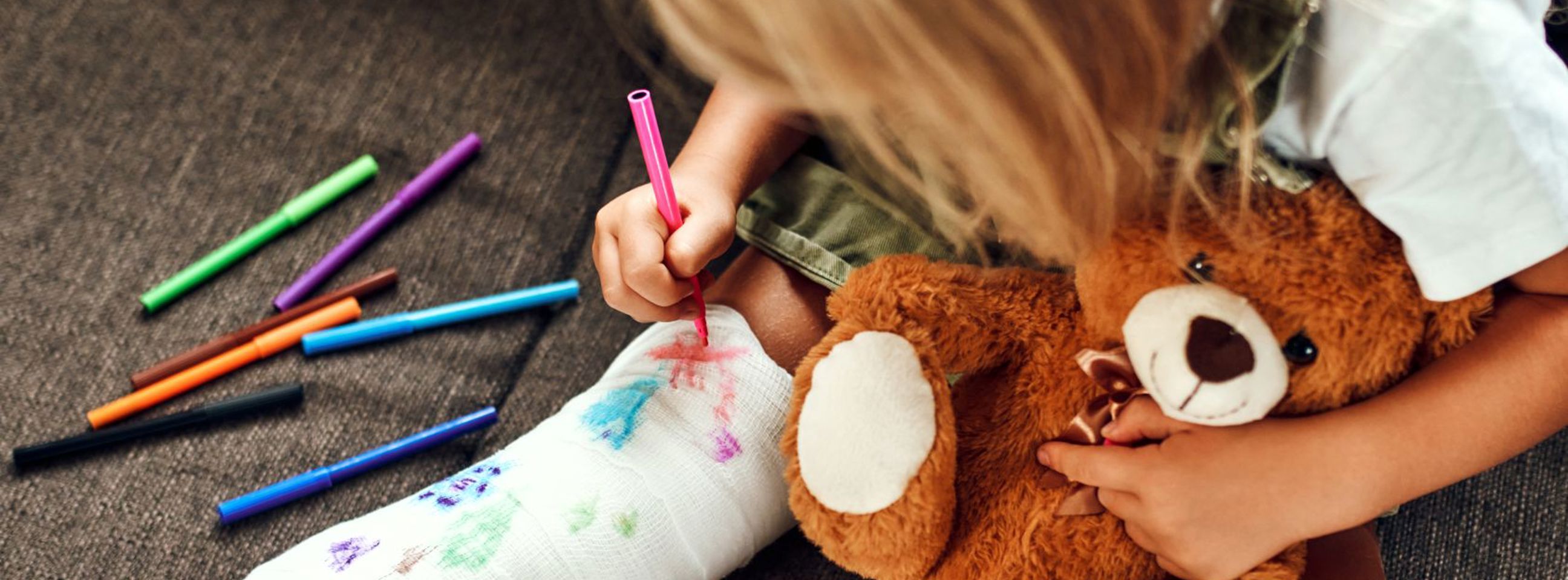 En lille pige med et brækket ben sidder i en sofa og tegner på gipsen