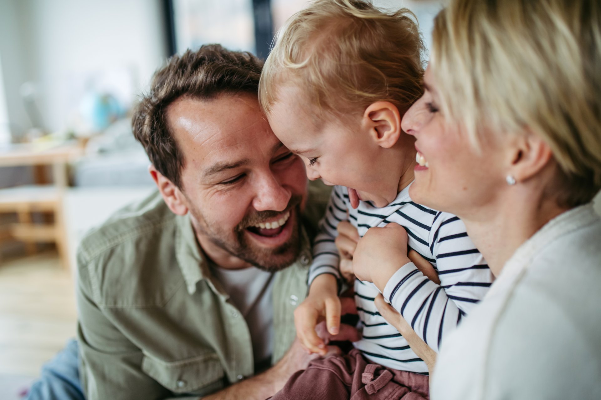 Far, mor og lille søn sidder sammen på gulvet og griner