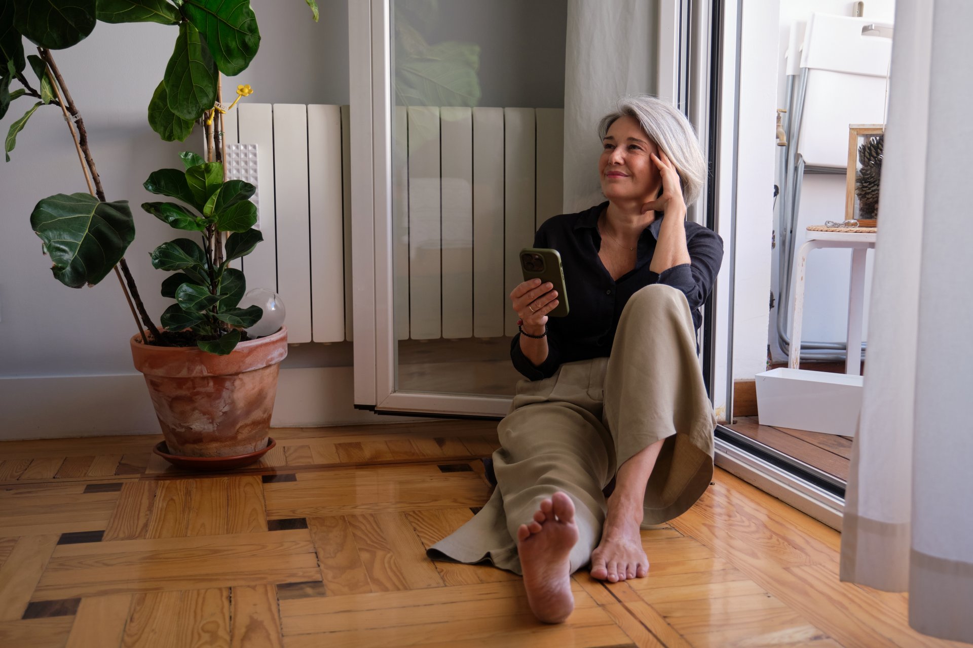 En kvinde sidder på gulvet i sit hus. Terrassedøren er åben, og hun sidder og nyder den friske luft fra haven.