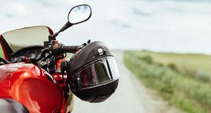 En rød motorcykel der holder stille, ved siden af åben mark en sommerdag. 