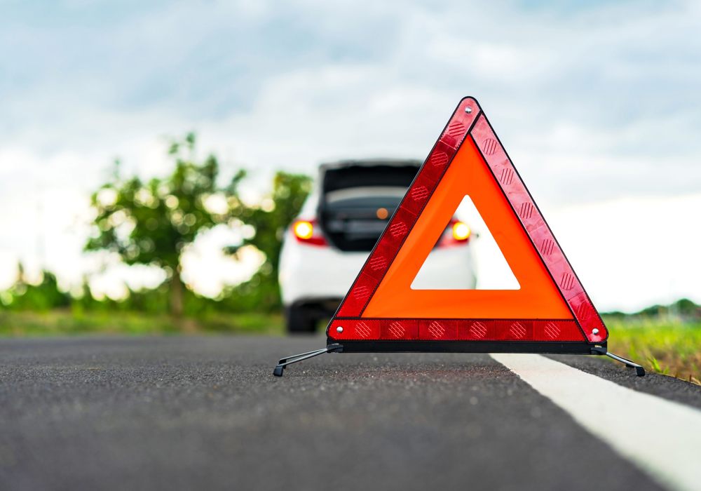Nærbillede af advarselstrekant. I baggrunden holder en hvid bil, der har brug for assistance.