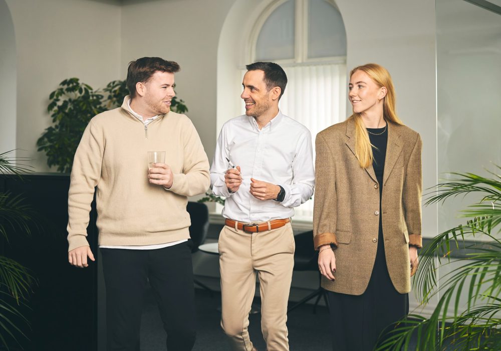 Tre kolleager går på række gennem kontoret og taler sammen
