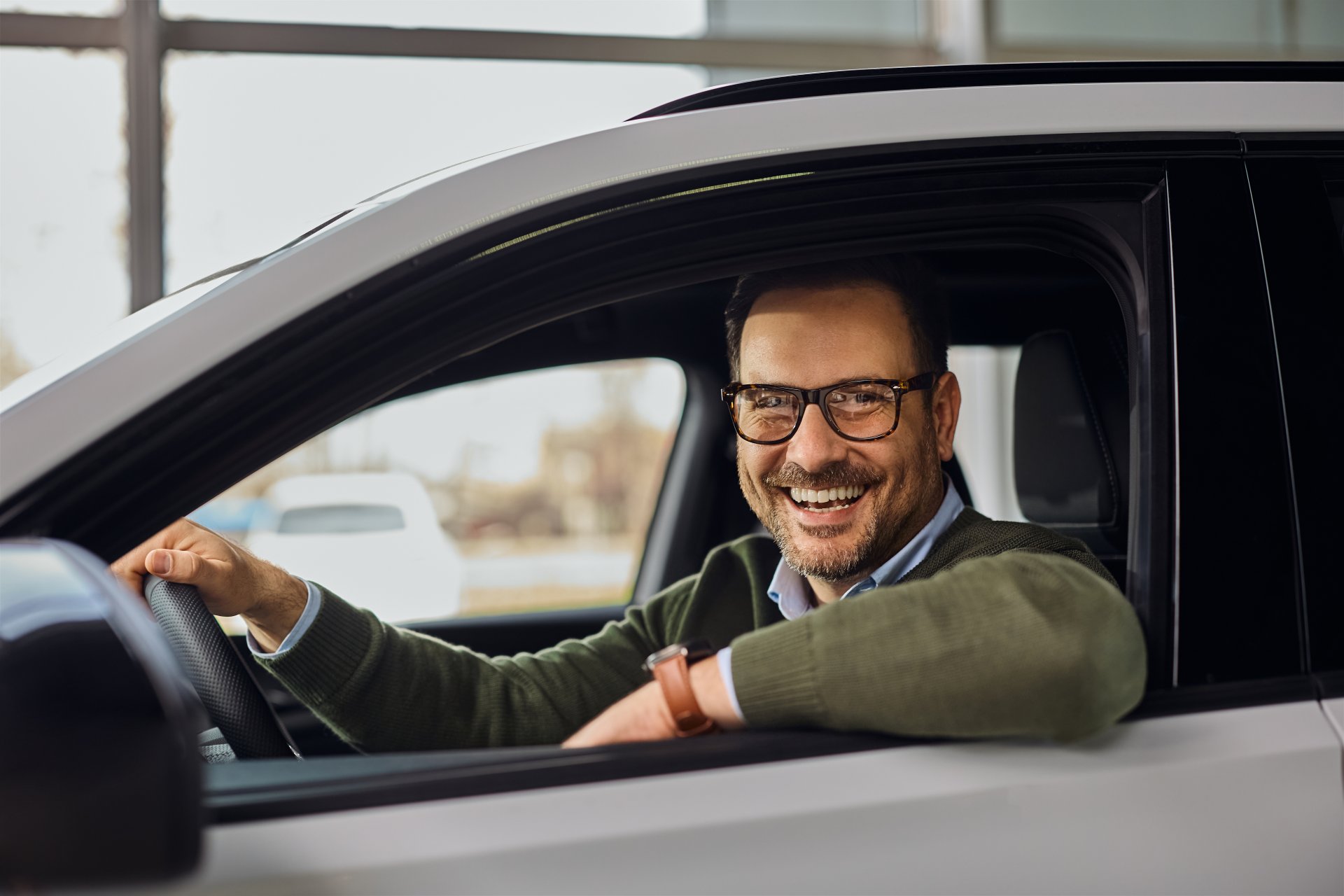 Smilende mand sidder bag rattet i en bil – illustration til gode råd om forsikring ved køb og salg af bil