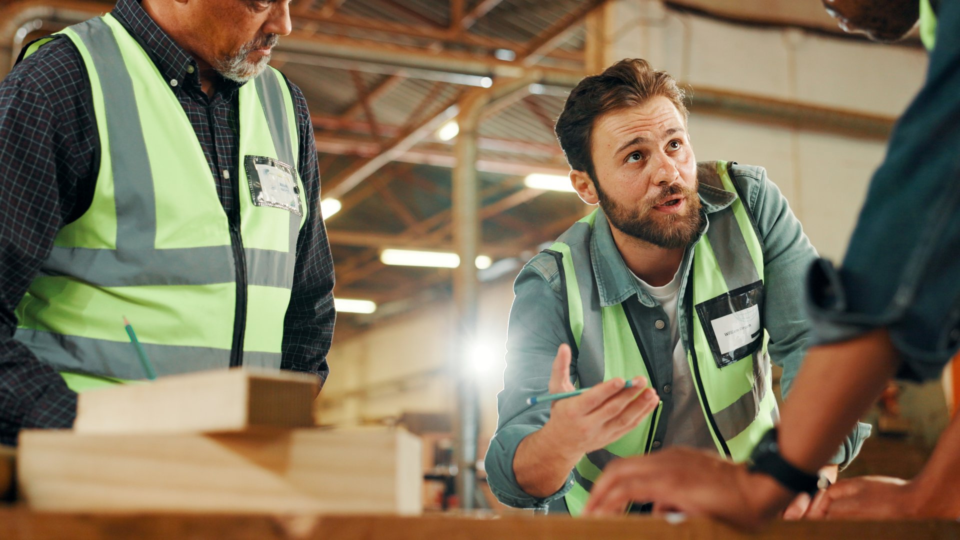 Medarbejdere i dialog om arbejdsopgaver i produktionshal – illustrerer erhverv og tryghed i hverdagen.