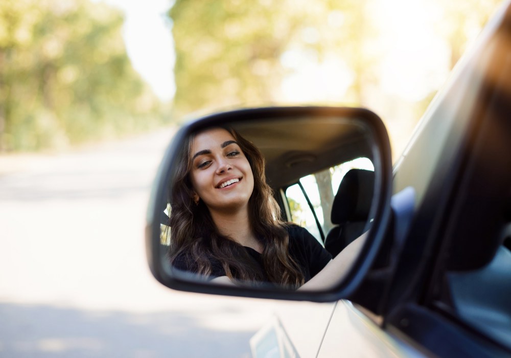 Ung kvindelig bilist kigger i sidespejlet - kørekort som 17-årig.