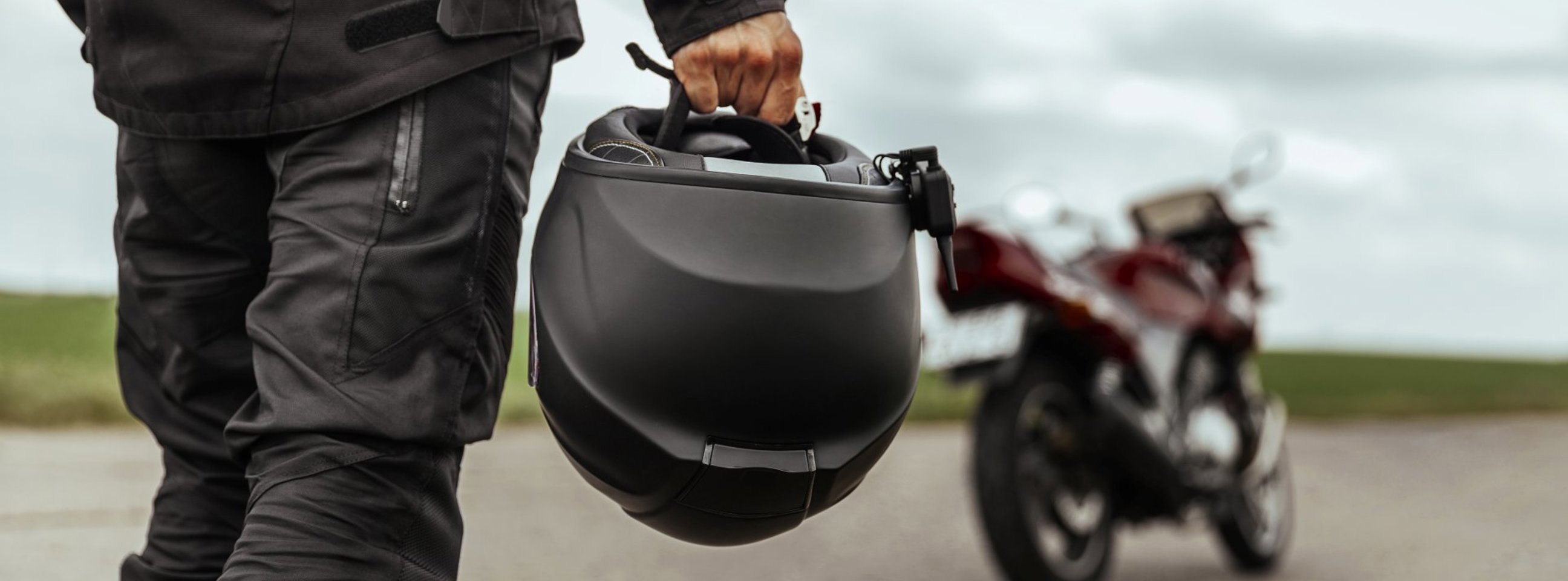 Nærbillede af en mand, som holder en styrthjelm i hånden - bagved står hans motorcykel