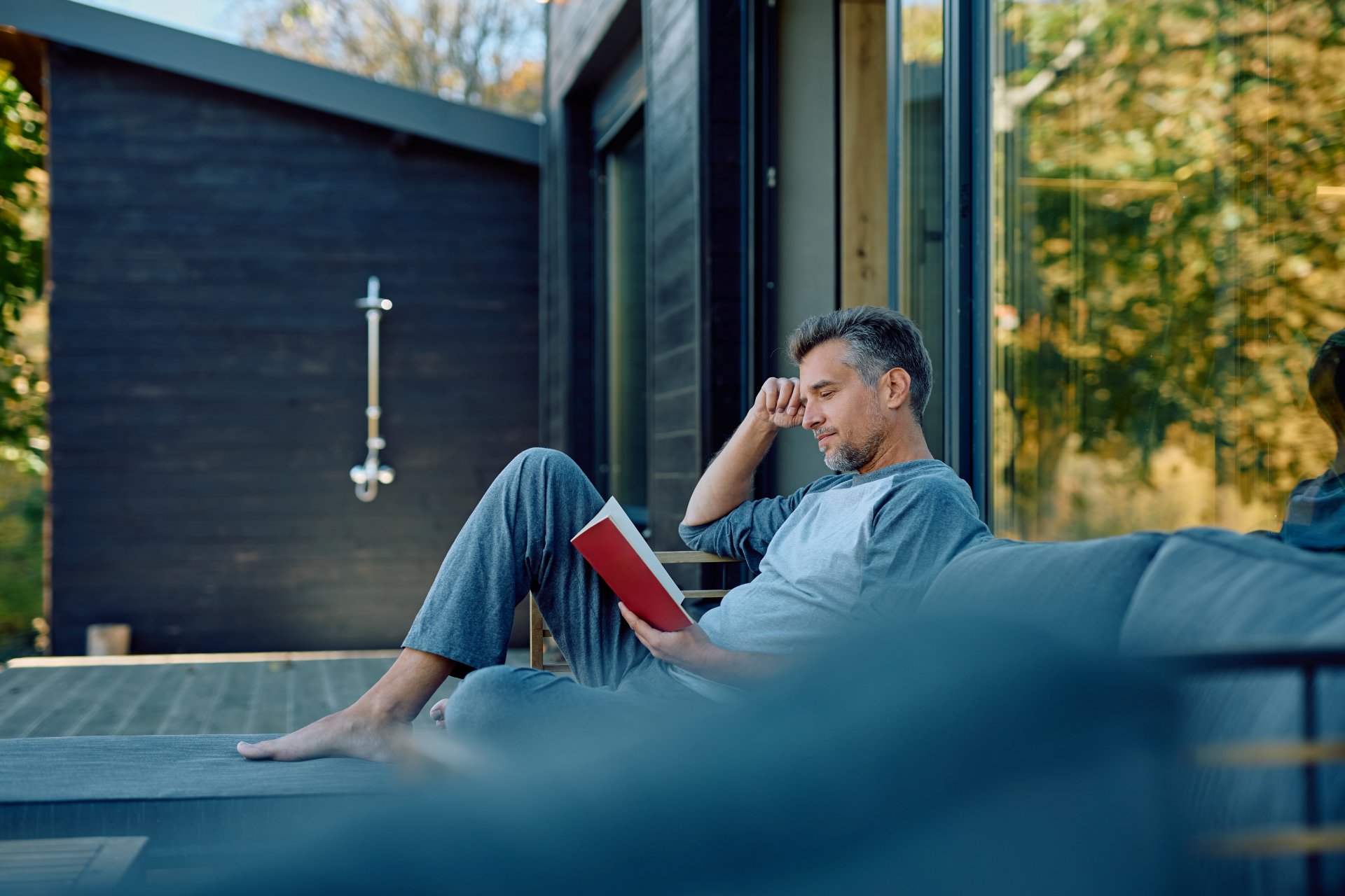 Mand sidder på terrassen ved sit sommerhus og læser en bog