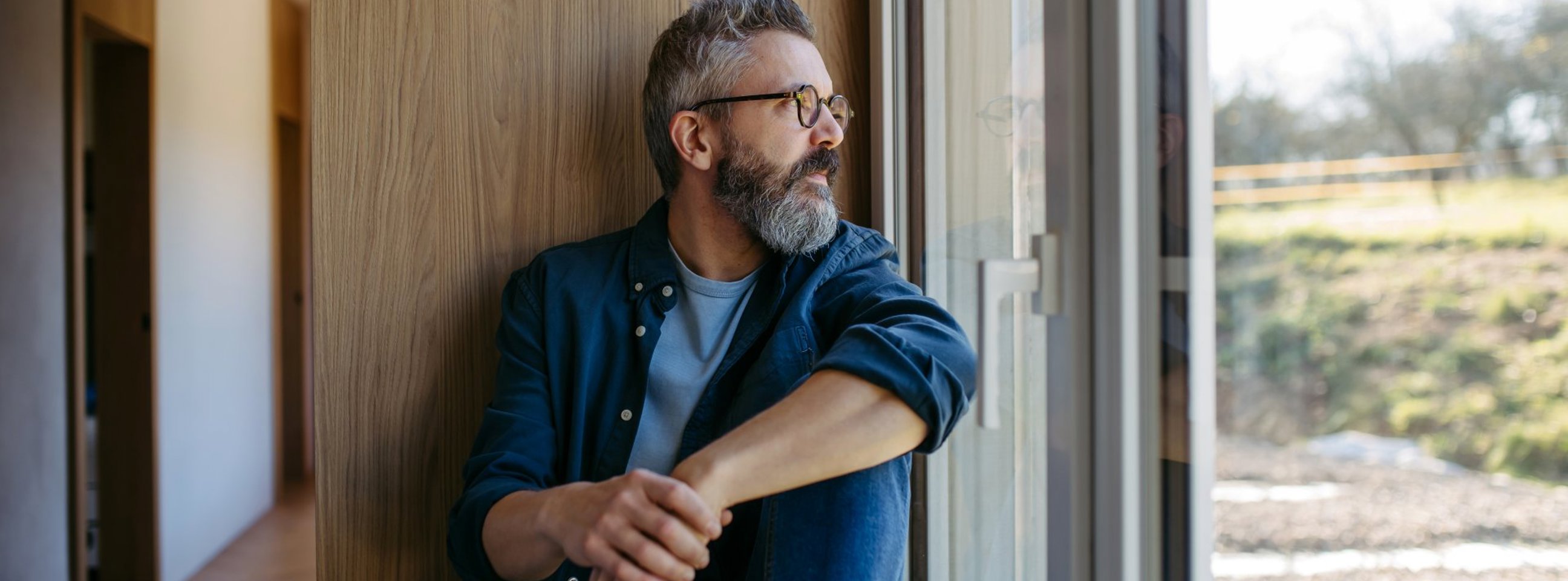 En mand sidder i sit nybyggede hus og kigger ud ad vinduet mod haven