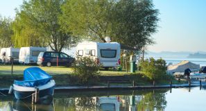 Campingvogn der holder ved en sø, med omkringliggende træer og andre campingvogne.