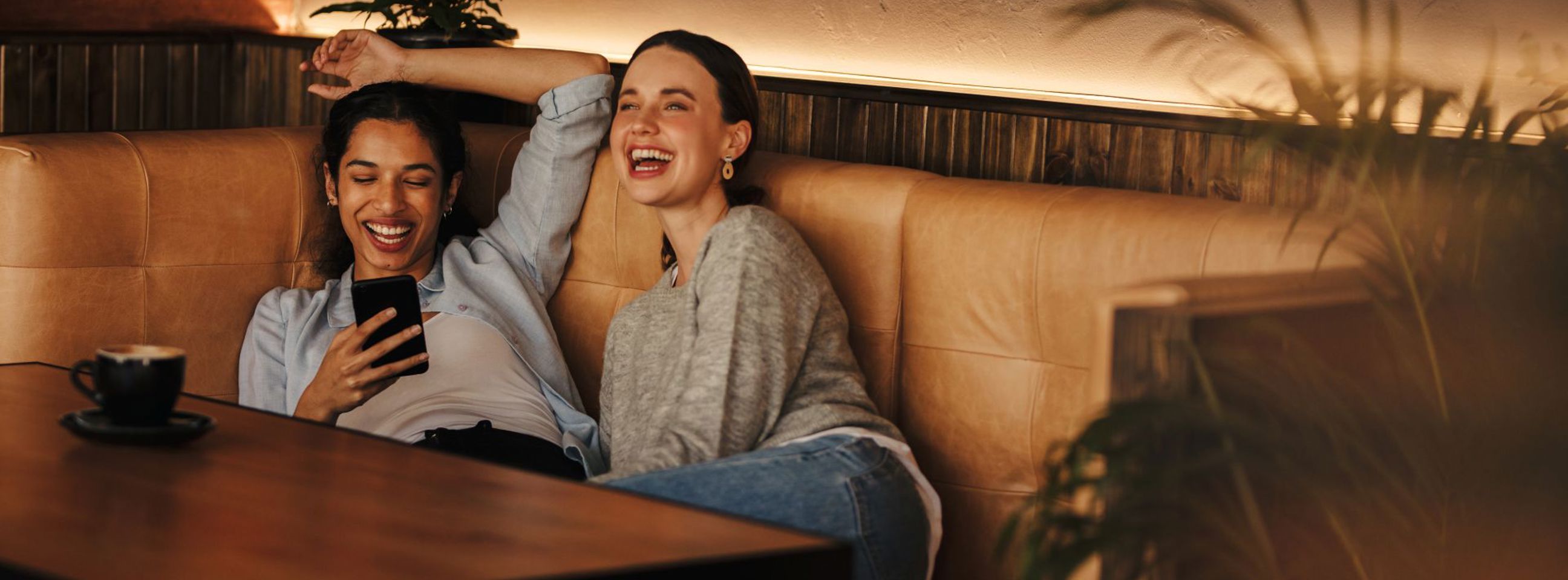 To unge kvinder sidder på en café og griner sammen