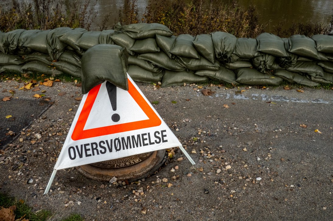 Advarselstrekant sat op i forbindelse med stormflod og oversvømmelse. Bagved ligger stablede sandsække for holde vandet væk.